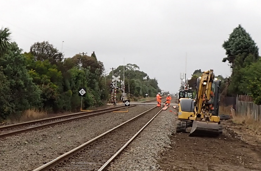 Workers in orange high-vis on a train track near a level crossing