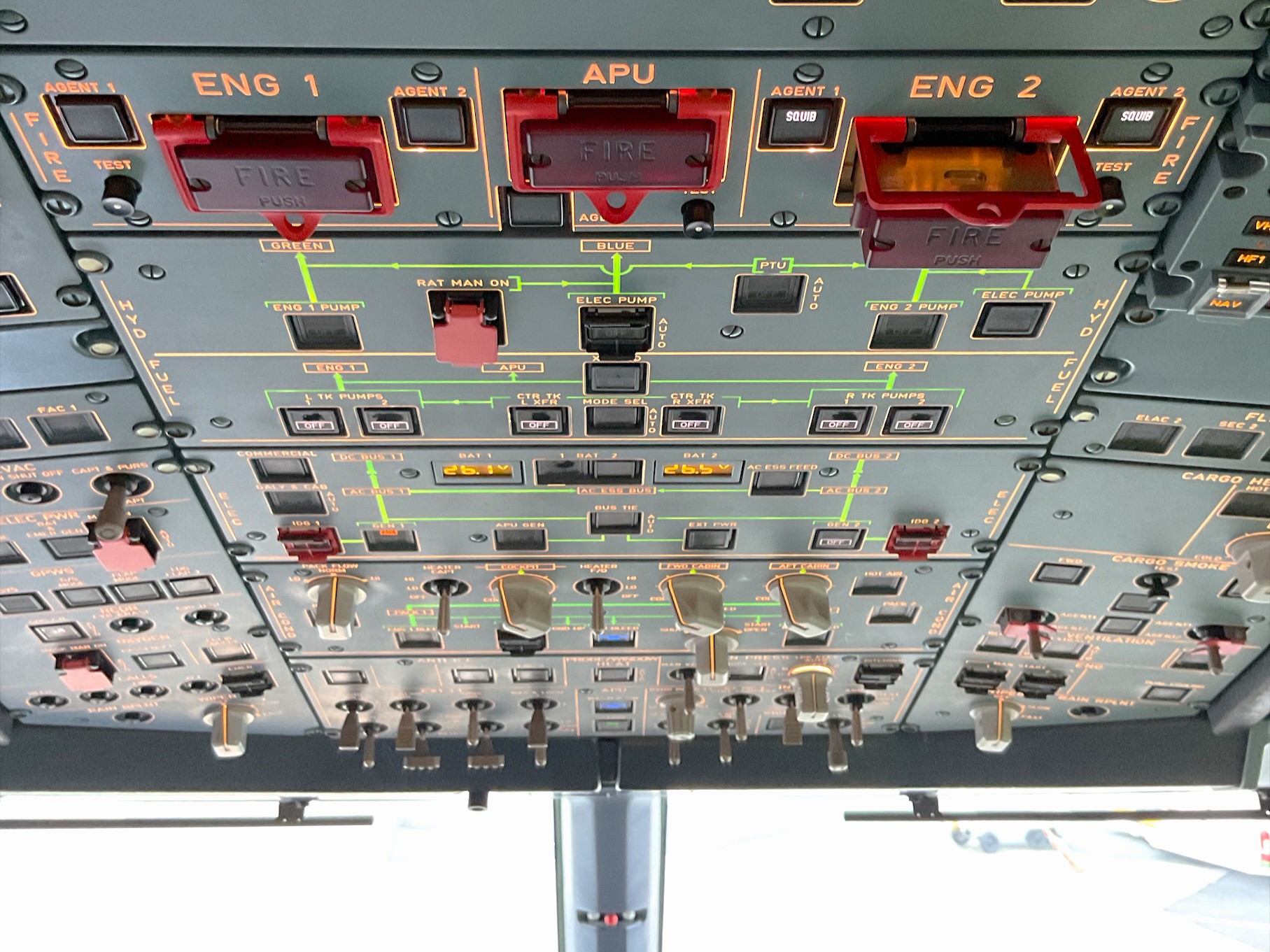Photo taken in the cockpit of an A320 from behind the pilot seats, looking forward, showing the overhead control panel. Nearest the viewer at the top of the photo is the fire control panel for Engine 1, auxiliary power unit and Engine 2. The push-release fire control switch for Engine 2 is in the ‘popped-out’ activated position. Beyond the fire panel are panels for hydraulics, fuel, electrical, with illuminated indicators, guarded switches, rotary selectors, and other controls, standard A320 layout.