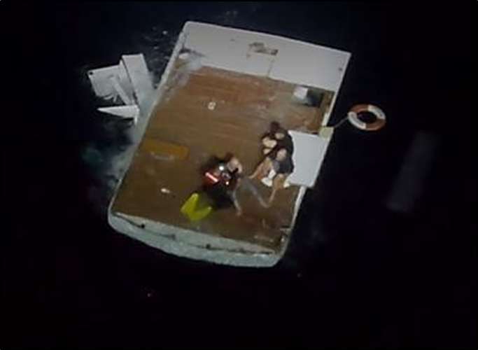 The inverted flybridge with a rescue swimmer and three survivors sitting atop what had been the ceiling of the main saloon and the floor of the flybridge