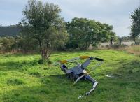 The accident  - wreckage. image depicts the helicopter wreck in a paddock beside the Arapito River. the fuselage is largely intact but bent in several places. the tail boom appears broken in several places, as do the main rotor blades, which ar still attached to the main rotor hub