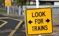 Photo of a level crossing with a road sign in the foreground, bearing 'Look for trains'