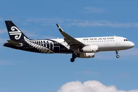 Air New Zealand Airbus A320 aircraft ZK-OXJ in flight with landing gear extended, approaching for landing against a blue sky. The aircraft features a distinctive black-and-white koru fern livery.