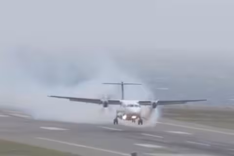 Front-on view of an Air New Zealand ATR72-600 twin-turboprop aircraft (ZK-MVL) on final approach to Wellington Airport on 1 September 2024. The plane is low over the runway with its landing gear down but not yet touched down. Dense grey-white smoke billows from the left engine, trailing back behind the aircraft, with the sea visible in the hazy overcast background beyond the runway