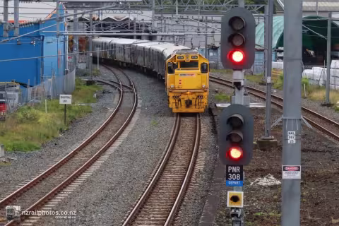 a passenger train stands stationary, across a set of points. In the foreground a rail traffic signal displays a red light. The parallel-converging track on the left is the one along which the metropolitan train was authorised to travel. 