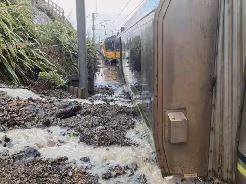 photo of accident scene. water rushes across landslip debris on to rail tracks. Carriages stand upright in the debris.